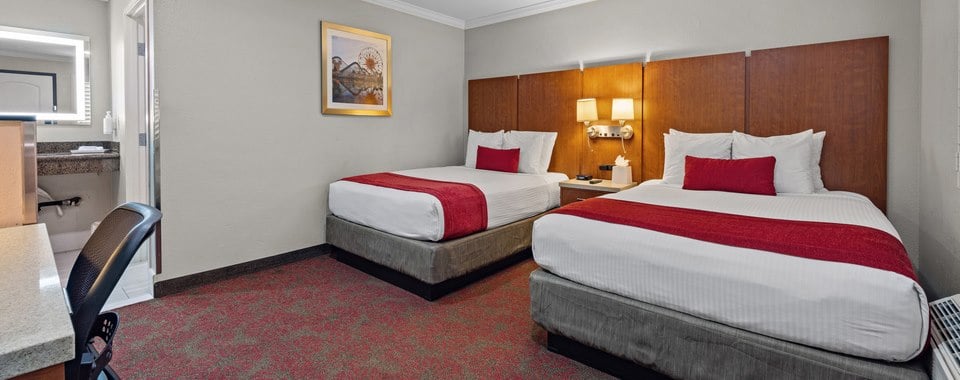 A hotel room with two beds, a nightstand, and a desk.