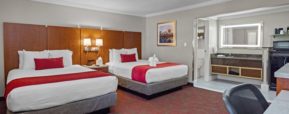 A hotel room with two twin beds, a desk, kitchenette, and bathroom