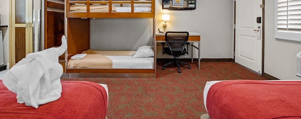 A hotel room with bunk beds, a desk, and a TV
